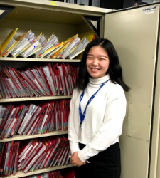 Student smiles in front of filing cabinet displaying files